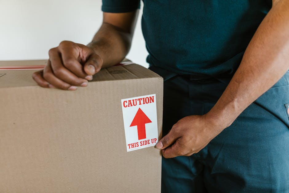 A large, wrapped piece of furniture, possibly a wardrobe or large box, secured with transparent plastic wrap for protection during a home relocation. The furniture is placed inside a room, near a door